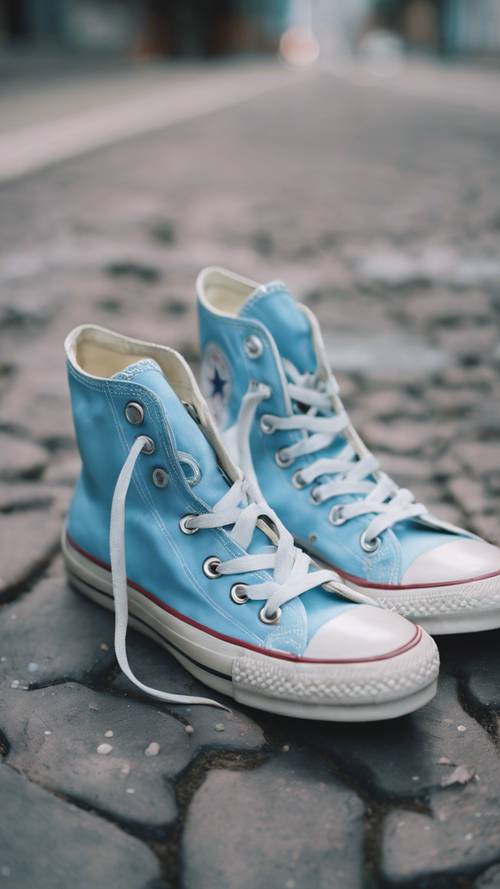 Tampilan dekat dari sepasang sepatu converse, dicat dengan warna biru pastel, berdiri di trotoar.