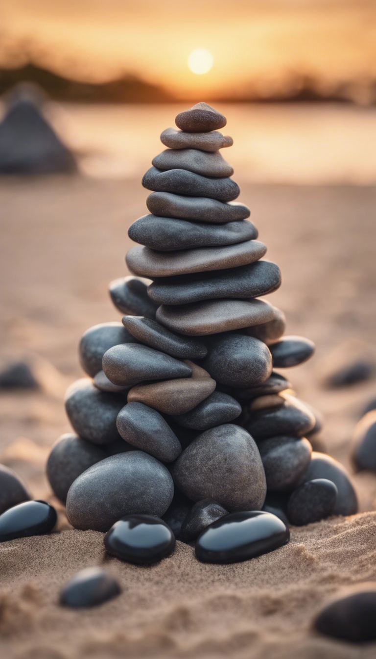 A pile of dark gray pebbles stacked in the shape of a pyramid on a sandy beach at sunset. Tapeta[d6df51511e664c29be44]