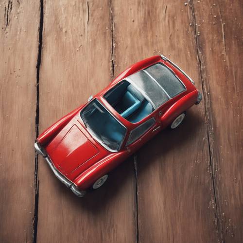 Красная игрушечная машинка, стоящая на пыльном деревянном полу, вид сверху.