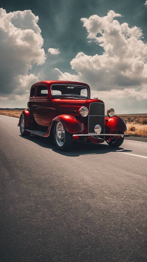 A red hot rod with black tinted windows against a backdrop of an open highway and big sky.