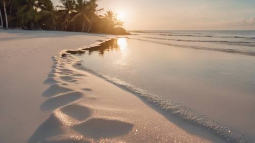 Pemandangan pantai pasir putih yang tenang memantulkan cahaya perak matahari terbenam.