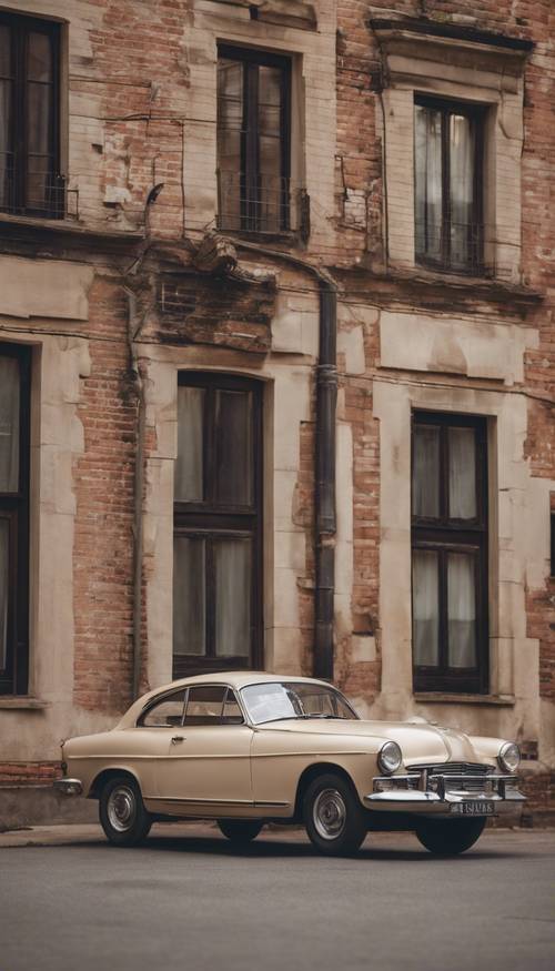 Jasnobeżowy, zabytkowy samochód zaparkowany przed starym ceglanym budynkiem