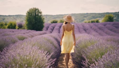 Eine junge Frau in einem pastellgelben Sommerkleid geht durch ein Lavendelfeld.