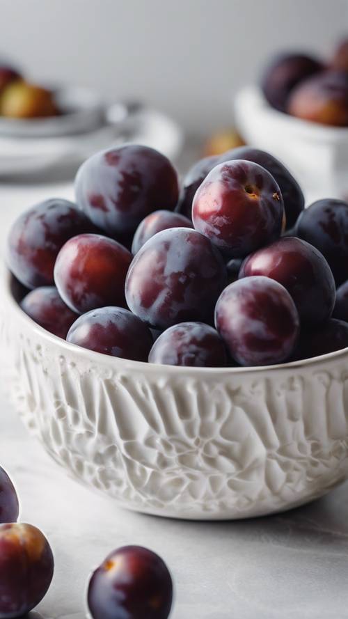 A handful of freshly picked plums in a white ceramic bowl on a kitchen counter.