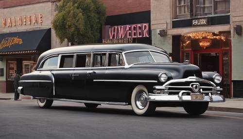 A classic 1950s hearse parked outside a vintage movie theater showing a Halloween double-feature.