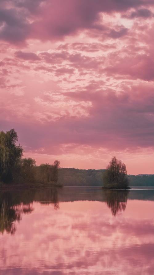 A picturesque view of a calm lake reflecting fluffy pink clouds at sunrise.