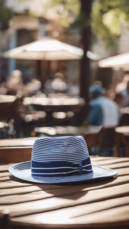 Un sombrero fedora de rayas azules y blancas sobre una mesa en un café callejero iluminado por el sol.