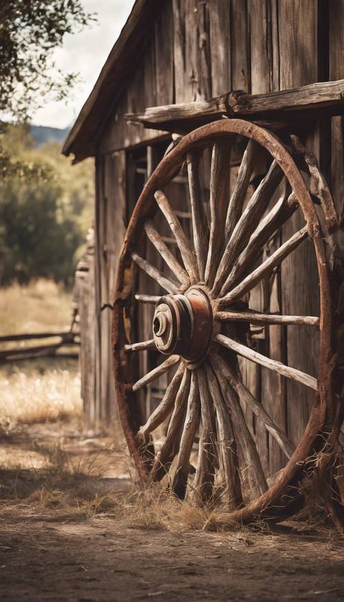 A rusted western wagon wheel leaning against an old barn