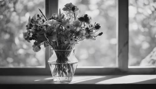 A black and white still life of a bouquet of various flowers in a glass vase.