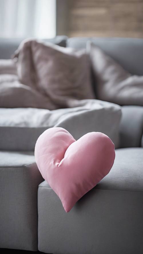 Bantal berbentuk hati berwarna merah muda dengan santai dilempar ke atas sofa abu-abu.