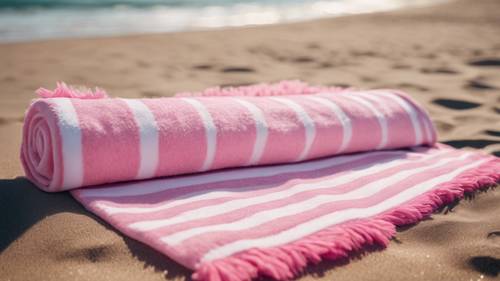 Ein kaugummirosa-weißes Streifenmuster auf einem flauschigen Strandtuch, das auf goldenem Sand ausgebreitet ist.