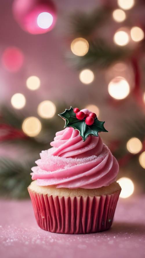 A close-up of a pink Christmas cupcake with sugar frosting and a holly decoration.