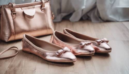 Um par de sapatilhas na cor ouro rosa metálico, ao lado de uma bolsa combinando sobre um piso de madeira.