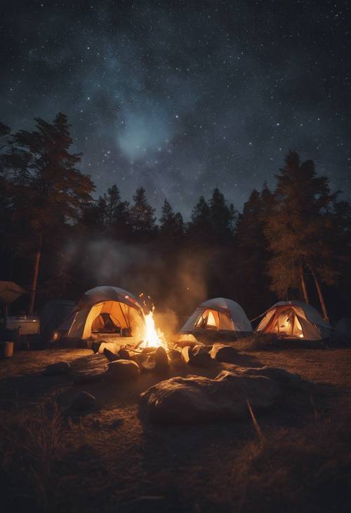 Scenic view of a summer campsite at night, showcasing a blazing campfire surrounded by tents under the open starlit sky.