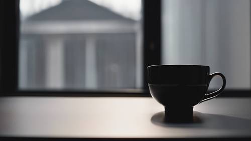 A solitary black teacup on a dark, minimalist kitchen countertop reflecting the muted light from a window.