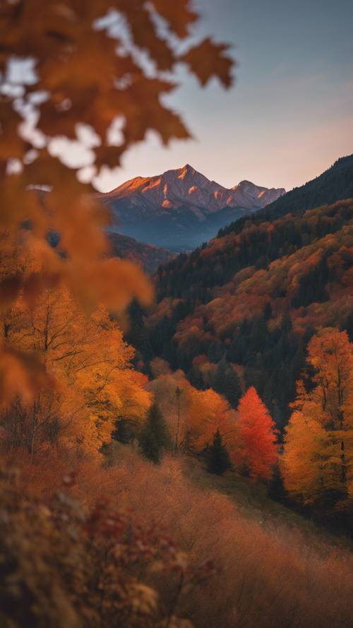 A mountain range bursting with fall colors under a twilight sky.