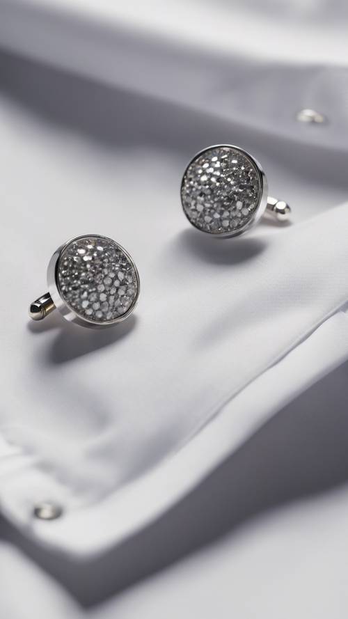 Um par de abotoaduras cinza cravejadas de diamantes em uma camisa branca impecável.