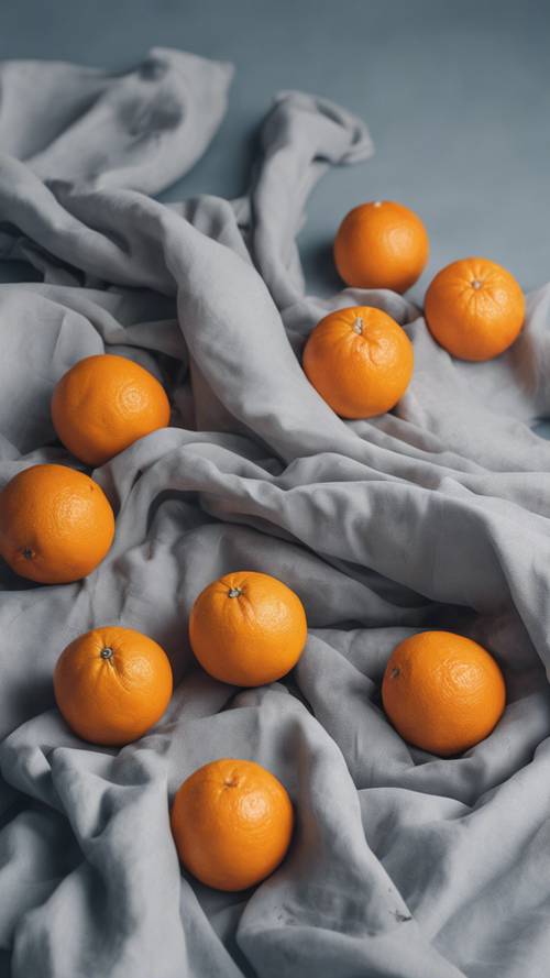 Un gruppo di arance sparse artisticamente su un panno bianco con uno sfondo blu-grigiastro che ricorda un dipinto di natura morta.