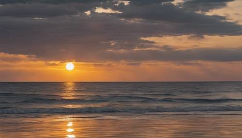 Um sol dourado a pôr-se sobre o mar calmo e cinzento, criando um magnífico jogo de cores.