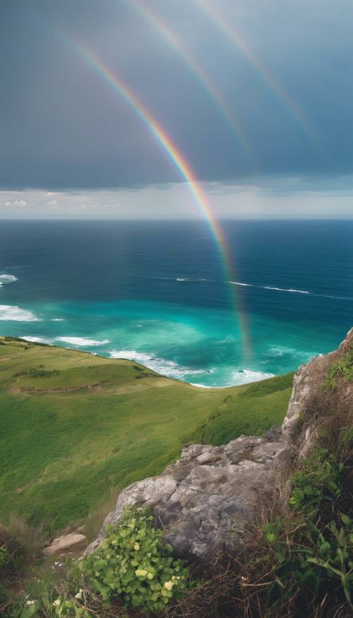 Яркая голубая радуга, видимая с вершины скалы, на фоне зеленых лугов и океана.
