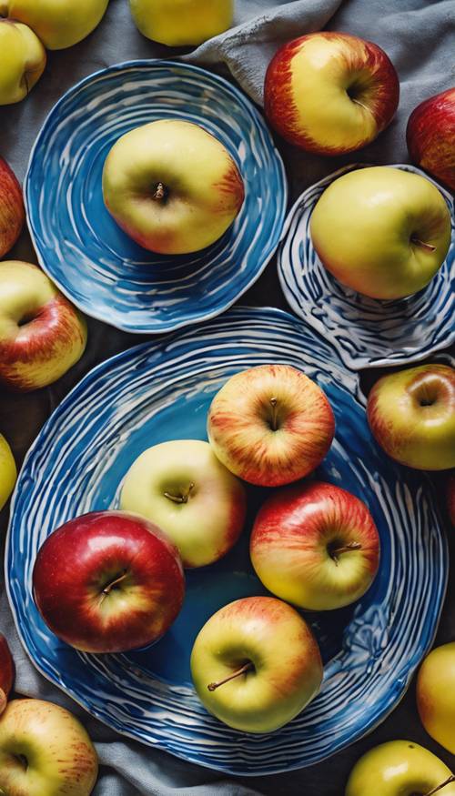 Parlak mavi seramik tabak üzerinde sanatsal bir şekilde düzenlenmiş, koyu kırmızıdan sarıya ve çizgiliye kadar çeşitli elmalar.