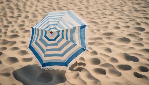 Parasol plażowy w biało-niebieskie paski na piasku skąpanym w blasku słońca. Tapeta [da561a4fef924e4fa43e]