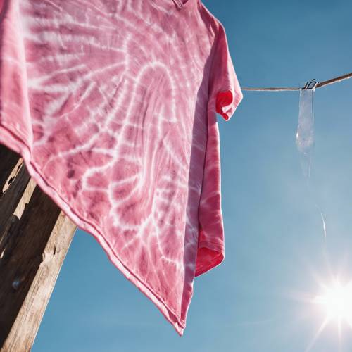 Ein selbstgemachtes rosa Batik-Shirt trocknet auf einer Wäscheleine vor einem klaren blauen Himmel.