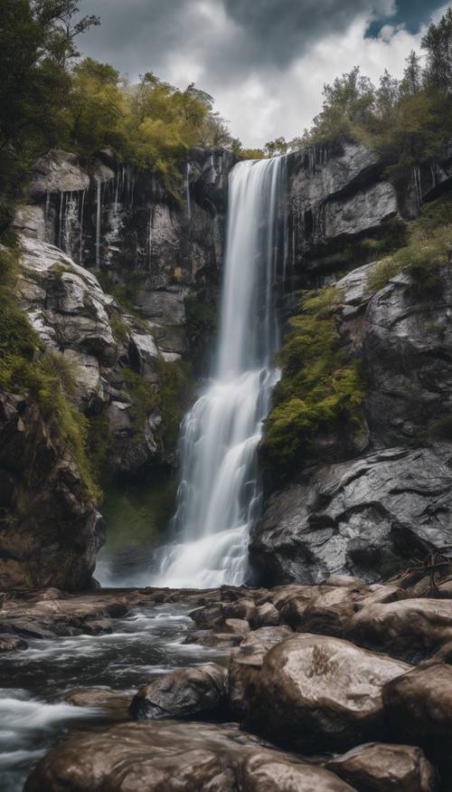 Ein silberner Wasserfall, der unter einem bewölkten Himmel über die Felsen stürzt.