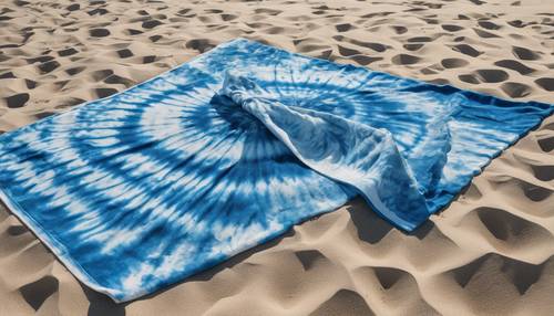 Kumlu plaja yayılmış canlı mavi batik bir plaj havlusu.