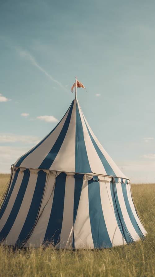 Ein gestreiftes Vintage-Zirkuszelt auf einer Wiese mit blauem Himmel darüber.