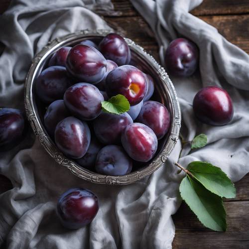 A bowl of ripe, glossy purple plums on a weathered silver tray.