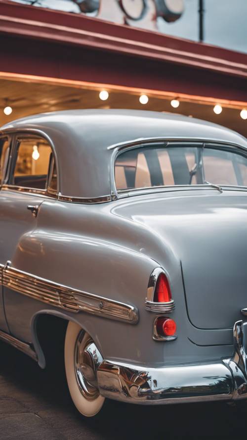 Une voiture vintage des années 1950, peinte en gris clair, garée devant un restaurant original en bord de route.