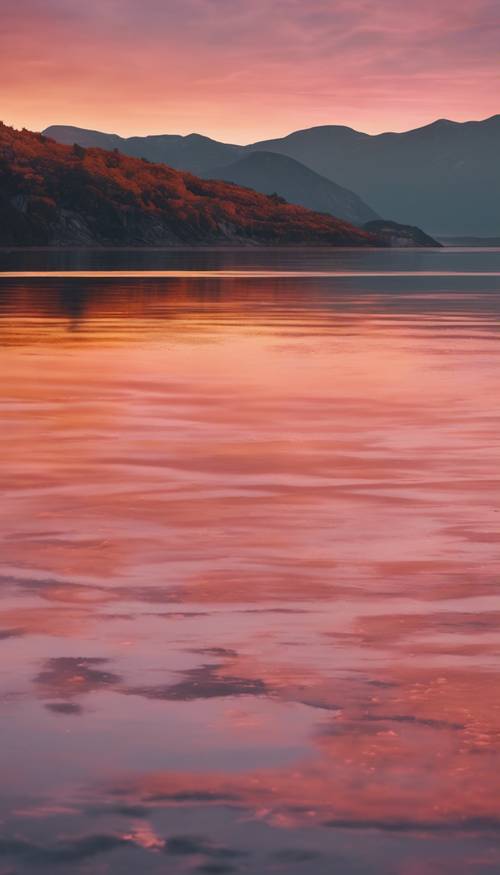 Sunset coloring the surface of a quiet fjord with orange and pink reflections