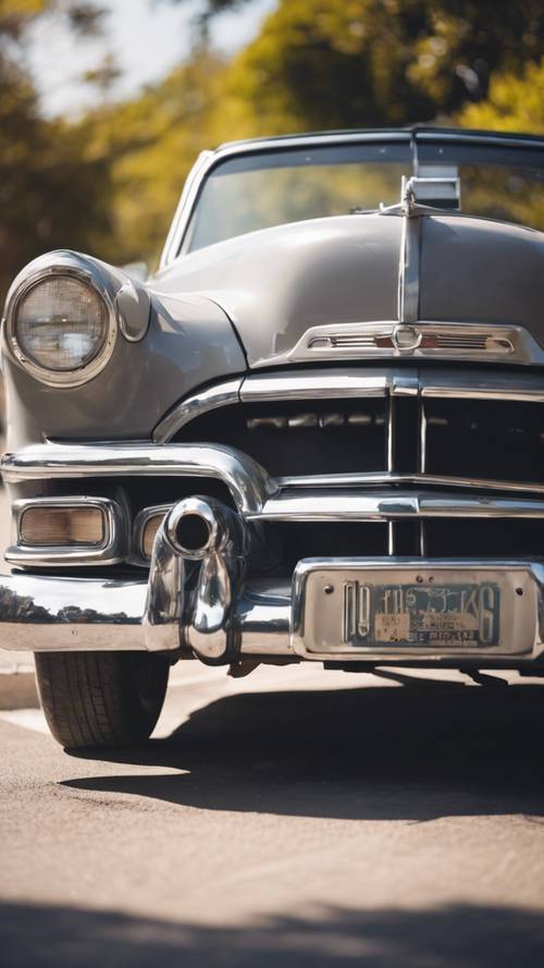 Ein graues Oldtimer-Cabrio, geparkt in einer amerikanischen Straße im Stil der 1950er Jahre in der hellen Mittagssonne.
