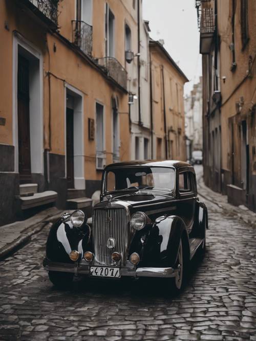 A classic black vintage car parked along a gloomy cobblestone street.