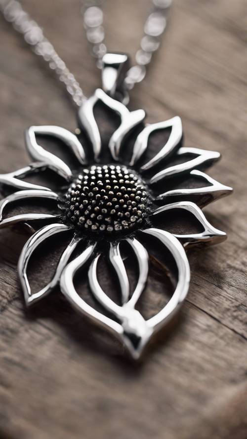 A dainty black sunflower pendant hanging on a silver chain against a rustic wooden table.