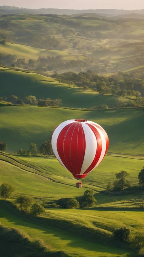 A red and white hot air balloon gracefully soaring over rolling green hills in the early morning light.