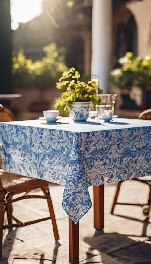 Tovaglia damascata blu e bianca drappeggiata su un tavolo da bistrot all&#39;aperto, il sole che irradia una calda luce.