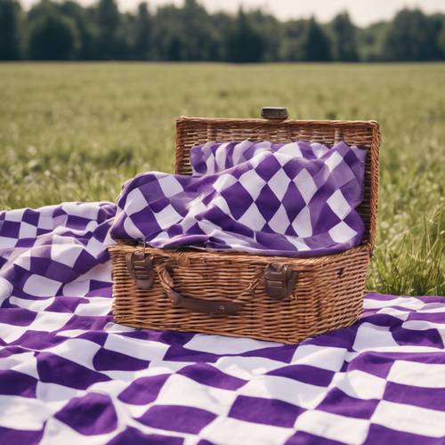 A preppy style, purple-and-white checkerboard picnic blanket spread on a sunlit field with a well-packed picnic basket at its center.