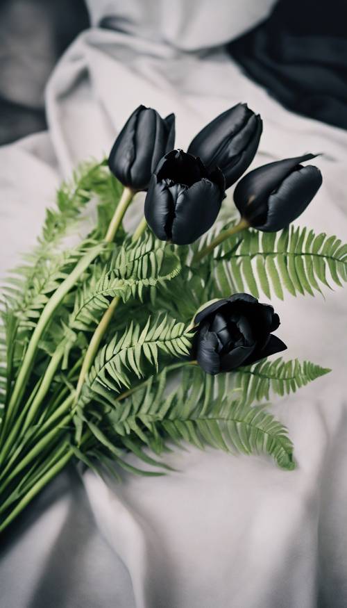 Un joli bouquet de tulipes noires disposées artistiquement avec des fougères vertes et enveloppées de soie noire.