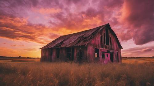 Uno splendido tramonto che dipinge il cielo con sfumature di rosa, arancione e oro sopra un fienile abbandonato.