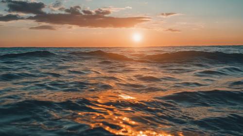 Scena zachodu słońca z pomarańczowym słońcem zachodzącym w chłodnym błękitnym oceanie.