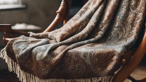 Um xale estampado antigo em tons suaves do sótão do vovô, pendurado sobre uma cadeira de balanço.