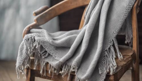 Écharpe en laine gris clair faite à la main drapée sur une chaise rustique en bois.