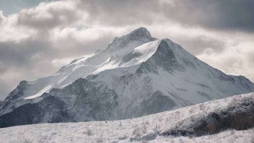 Sebuah gunung perak yang tertutup salju, berdiri tegak dengan latar belakang langit putih mendung.