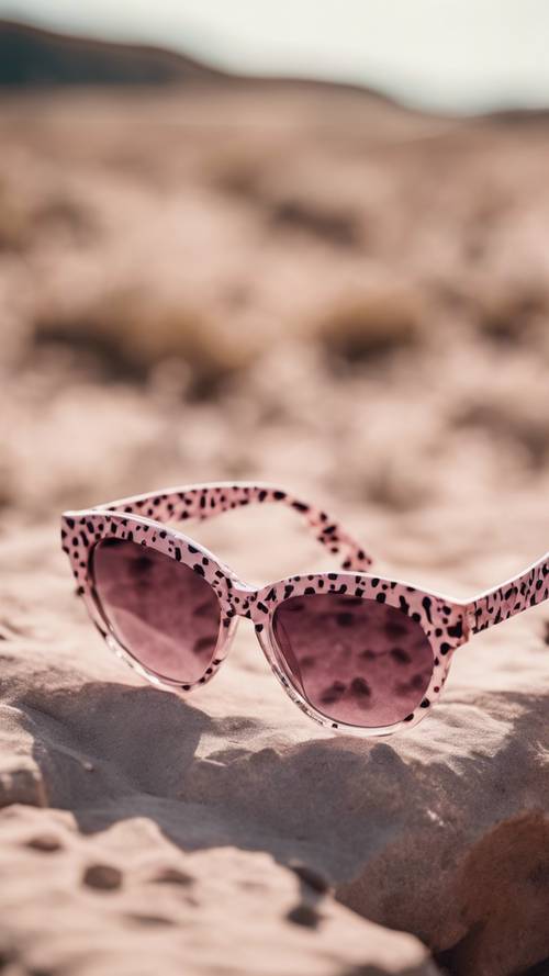 Sepasang kacamata hitam bergaya dengan bingkai bermotif bintik cheetah merah muda lembut.