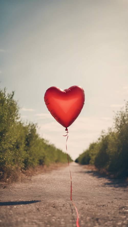 A classic red heart-shaped balloon floating freely against a clear, sunny sky.