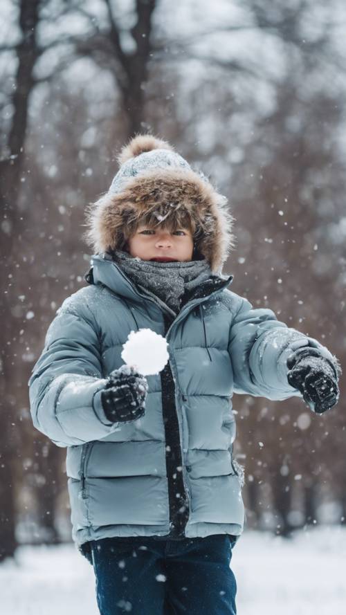 דיוקן של ילד מגניב בבגדי חורף, נשימתו גלויה באוויר הקר, כשהוא זורק כדור שלג בפארק מכוסה שלג.
