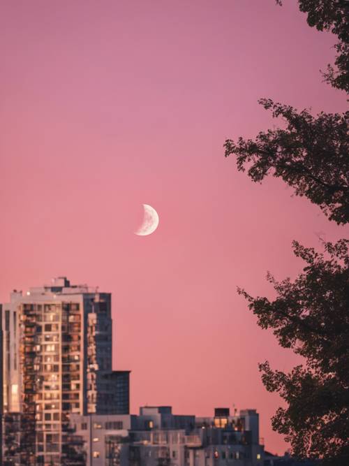 Luna creciente en un cálido cielo nocturno rosado, vista desde el horizonte de una ciudad.