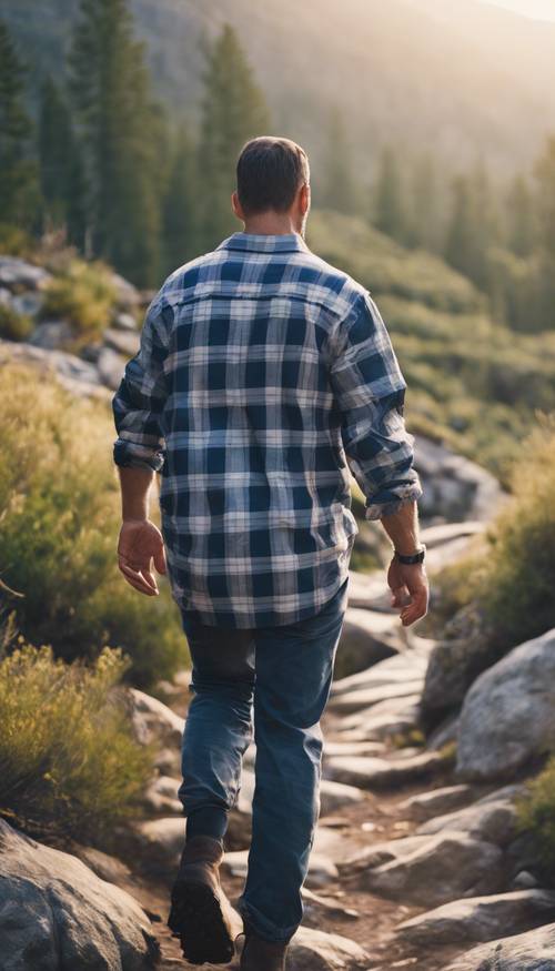 Um homem de trinta e poucos anos vestindo uma camisa de flanela xadrez azul e branca caminhando nas montanhas durante o início da manhã.